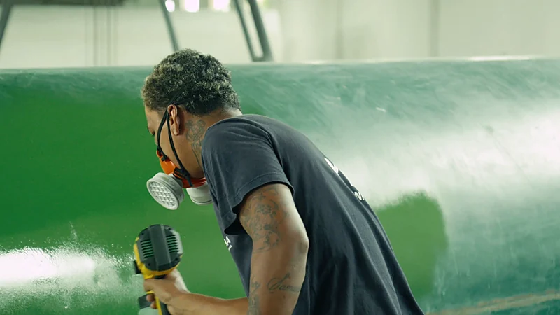Técnico com respirador aplicando o acabamento verde em um tanque horizontal