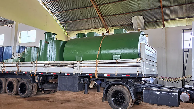 Carreta com tanques de PRFV verdes amarrados, saindo do galpão da fábrica